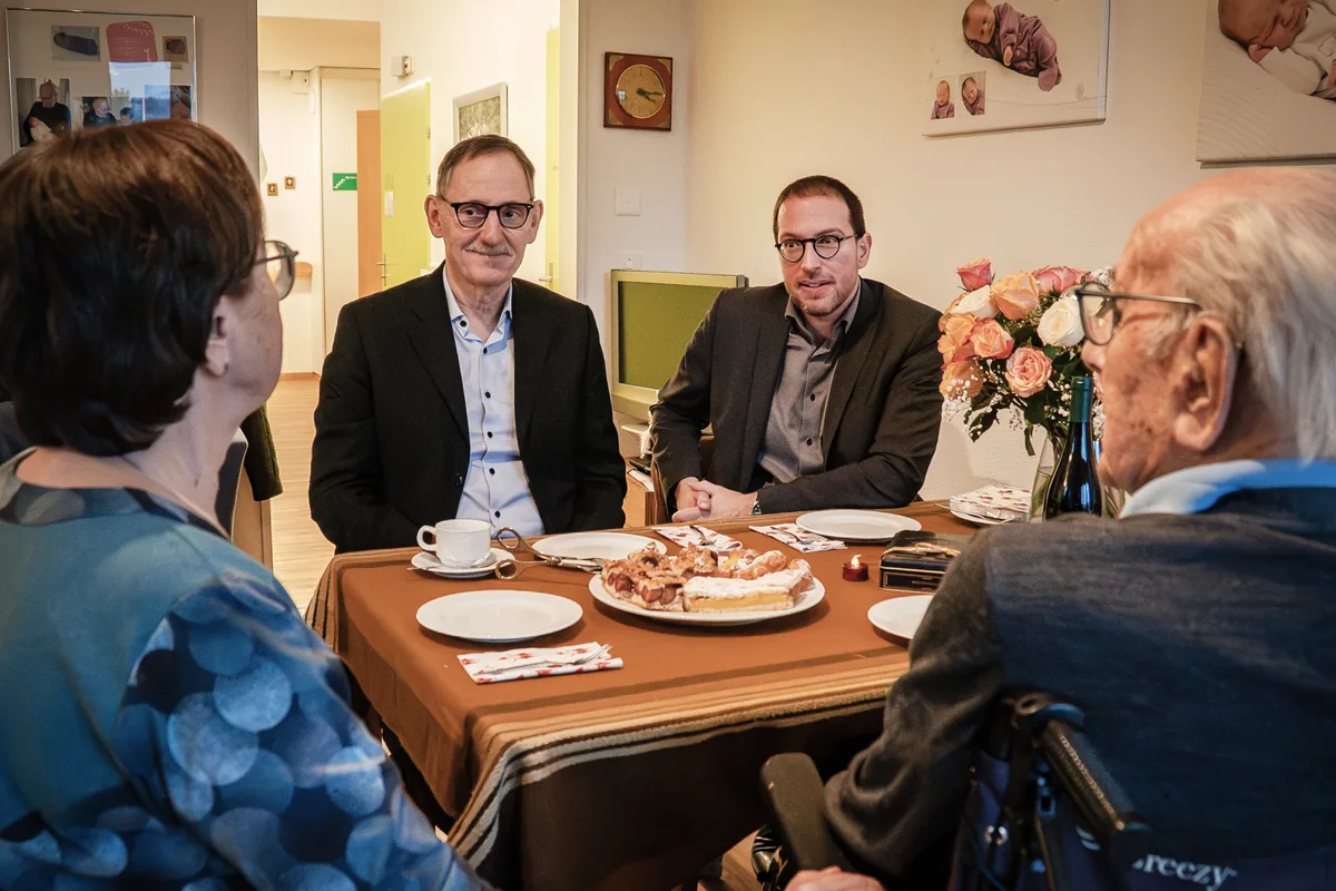 Die Politiker lauschen bei Kuchen den Geschichten des ältesten Schweizers in Uster. Mario Fehr und Daniel Frei sitzen an einem gedeckten Tisch.